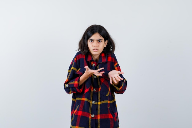 Foto grátis jovem, esticando as mãos de forma questionadora em camisa quadriculada e olhando perplexa, vista frontal.