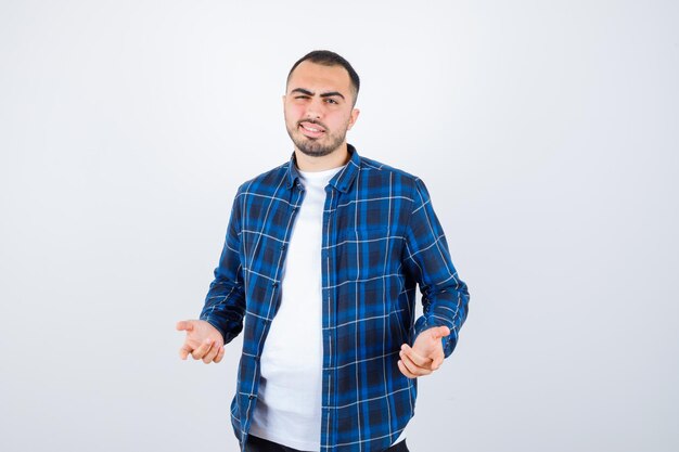 Jovem esticando as mãos de maneira questionadora, usando uma camisa xadrez e uma camiseta branca, parecendo perplexo