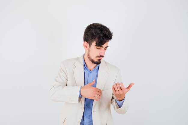 Foto grátis jovem esticando as mãos, segurando algo e olhando para ele com uma camisa azul e um paletó branco e olhando focado