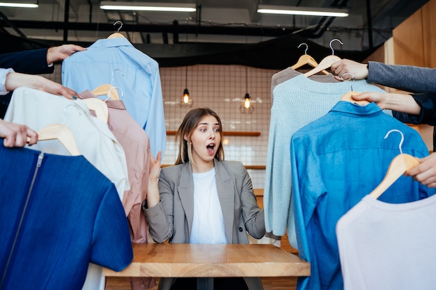 Jovem estilista olhando através de um conjunto de camisas para fotografar moda