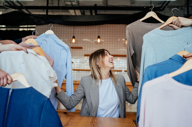 Jovem estilista olhando através de um conjunto de camisas para fotografar moda