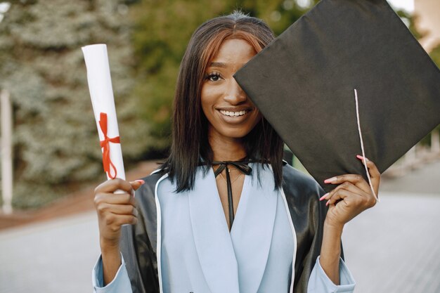 Jovem estudante afro-americana vestida com um vestido preto de formatura. Campus como pano de fundo