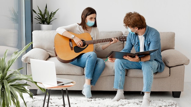 Jovem estudante aprendendo guitarra e vestindo máscara médica