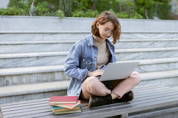 Jovem estudante bonita sentada com laptop garota caucasiana trabalhando ou estudando com notebook ao ar livre Foto Premium