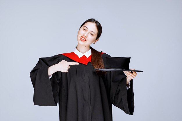 Jovem estudante em um vestido apontando para o cap. Foto de alta qualidade