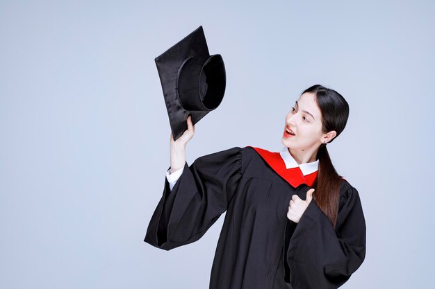 Jovem estudante em um vestido mostrando seu chapéu de formatura. Foto de alta qualidade