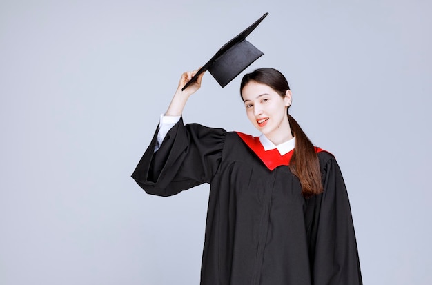 Jovem estudante em um vestido mostrando seu chapéu de formatura. Foto de alta qualidade