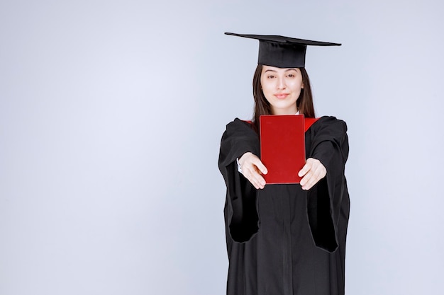 Jovem estudante em vestido acadêmico, mostrando o livro vermelho para a câmera. foto de alta qualidade