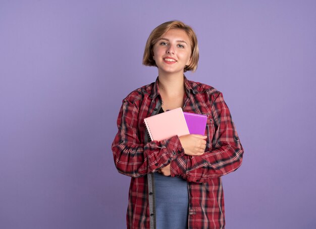 Jovem estudante eslava sorridente segurando um livro e um caderno