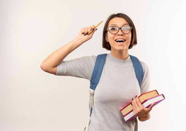 Jovem estudante impressionada de óculos e bolsa com as costas segurando livros e levantando a caneta isolada no branco