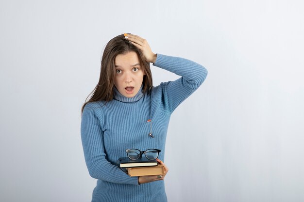 jovem estudante segurando livros e óculos.