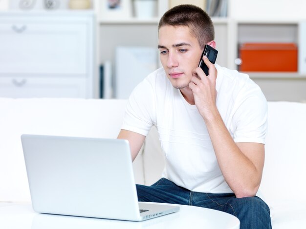 Jovem fala ao telefone e trabalha no laptop