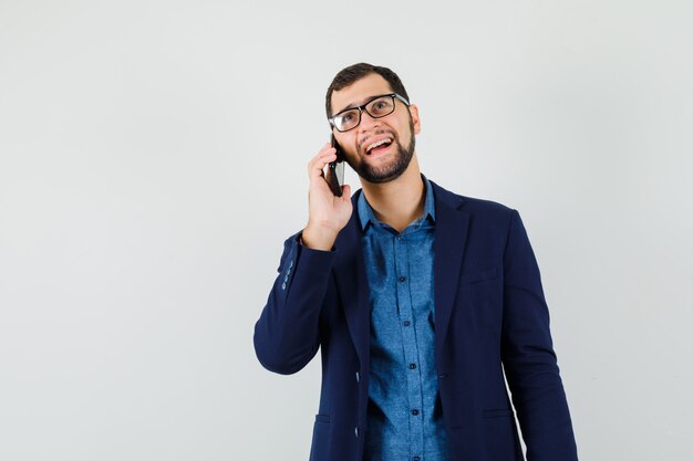 Jovem falando ao celular com camisa, jaqueta e parecendo alegre