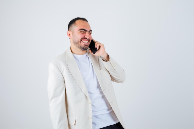 Jovem falando ao telefone em camiseta branca, jaqueta e parece feliz. vista frontal.