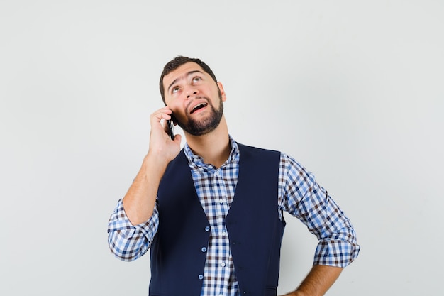 Foto grátis jovem falando no celular, com camisa, colete e parecendo pensativo.