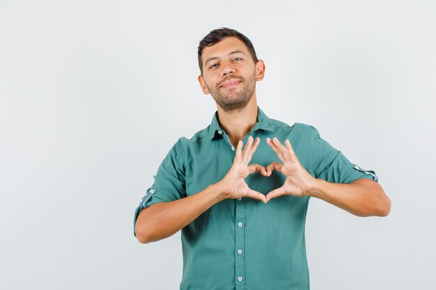 Jovem fazendo formato de coração com as mãos na camisa e parecendo amigável.