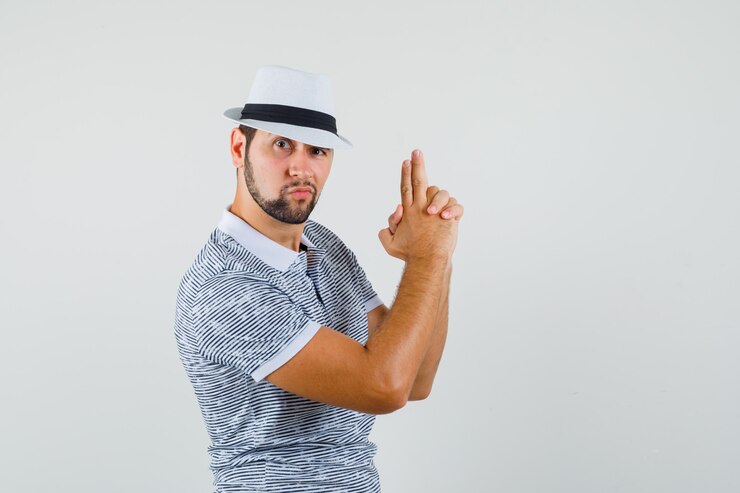 Foto grátis jovem fazendo gesto de arma de tiro em camiseta listrada, chapéu e parecendo corajoso. vista frontal.
