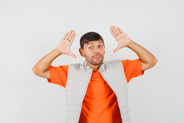 Jovem fazendo gesto de rendição em t-shirt, jaqueta, vista frontal.