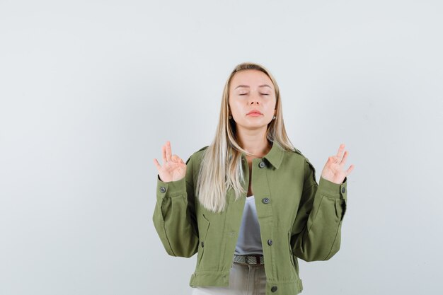 Jovem fazendo meditação com os olhos fechados, jaqueta, calça e parecendo relaxado. vista frontal.