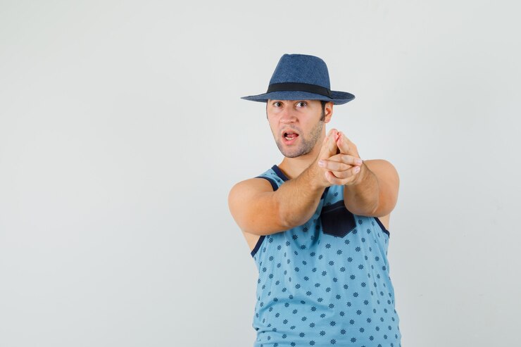 Foto grátis jovem fazendo sinal de pistola de dedo na camiseta azul, chapéu e parecendo confiante.