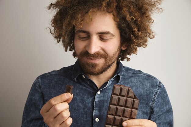 Jovem feliz barbudo com pele saudável e cabelo encaracolado, satisfeito com o sabor da barra de chocolate orgânico recém-assado