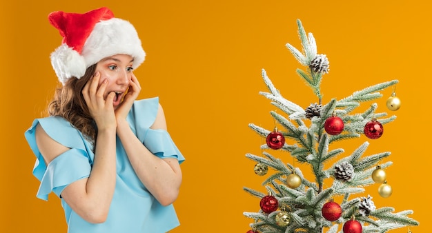 Jovem feliz com blusa azul e chapéu de papai noel usando óculos amarelos