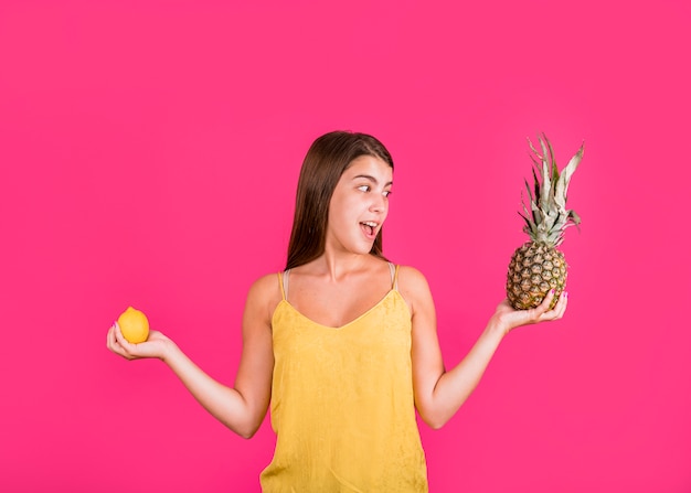 Jovem feliz com frutas exóticas se divertindo no fundo rosa