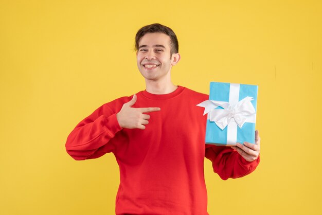 Jovem feliz com um suéter vermelho apontando para um presente sibilante em amarelo