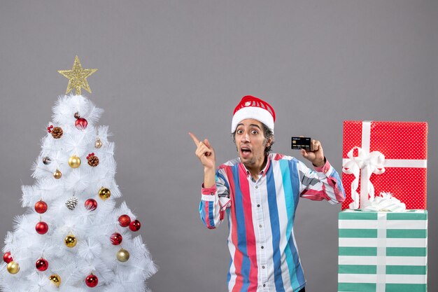 Jovem feliz de frente apontando o dedo mostrando a árvore de natal branca