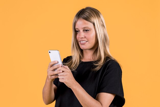 Jovem feliz desativar mulher usando telefone celular em fundo amarelo