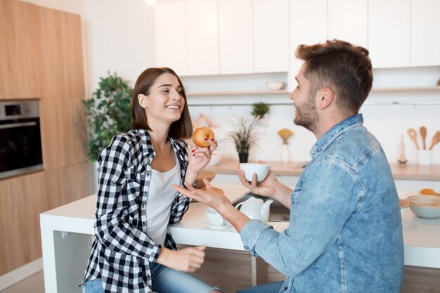 Jovem feliz e mulher na cozinha tomando café da manhã, casal juntos pela manhã, sorrindo, conversando