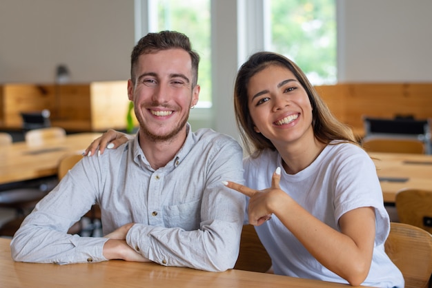 Jovem feliz e mulher sentada à mesa e posando para a câmera