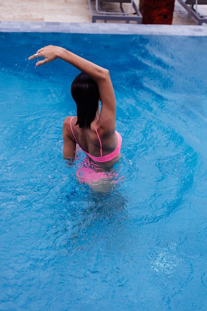 Jovem feliz em forma de mulher europeia magra em biquíni rosa brilhante azul piscina