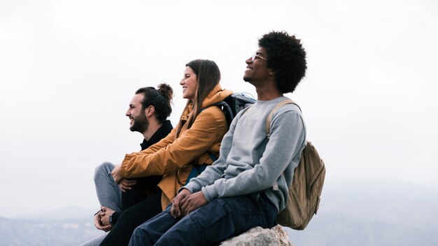 Jovem, feliz, macho fêmea, hiker, sentando, ligado, rocha, contra, céu