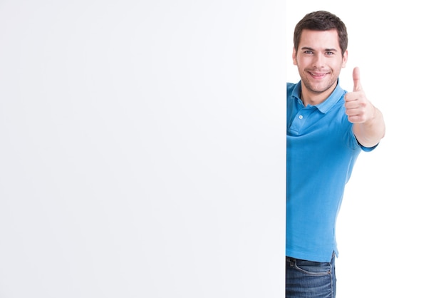 Jovem feliz olhar para fora do banner em branco com o polegar para cima - isolado no branco.