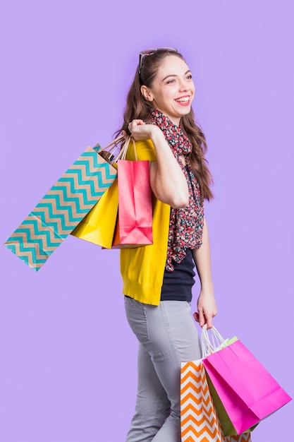 Foto grátis jovem feliz segurando sacolas de compras em pé contra a superfície de lavanda