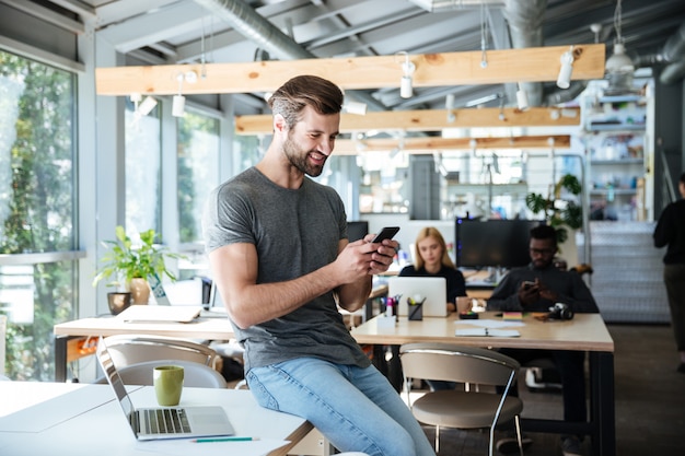 Foto grátis jovem feliz sentado na mesa no escritório conversando