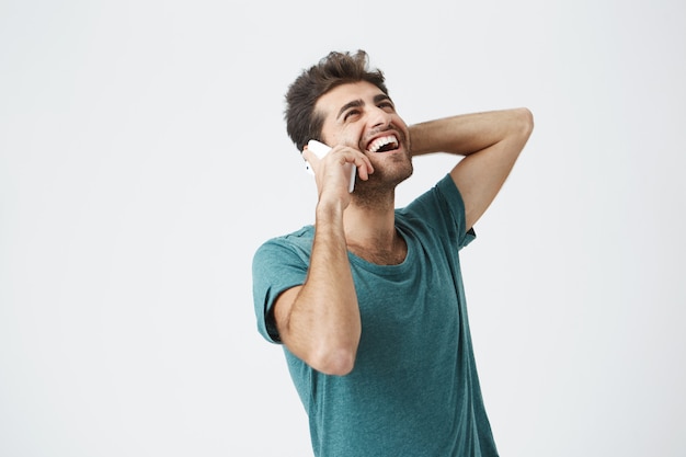 Jovem feliz sentindo animado, feliz e rindo enquanto fala ao telefone. hipster elegante se comunicando com a namorada por telefone inteligente com sorriso