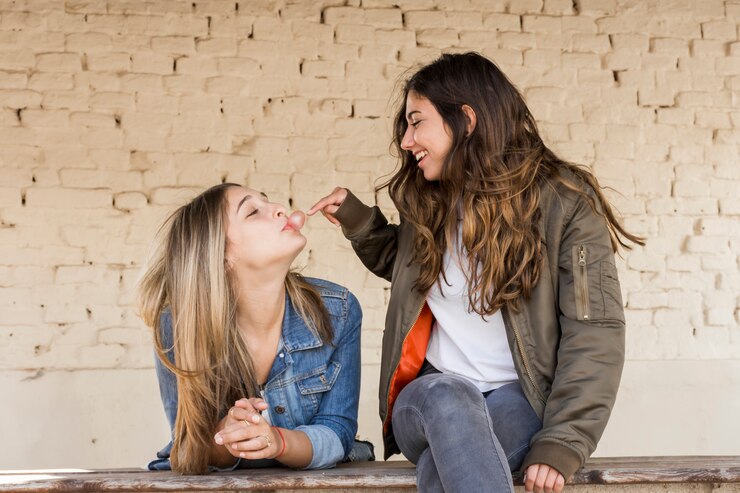 Foto grátis jovem feliz tocando uma bolha soprada por sua amiga com goma de mascar