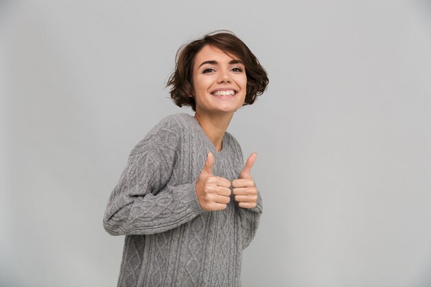 Jovem feliz vestida de suéter mostrando os polegares para cima gesto.