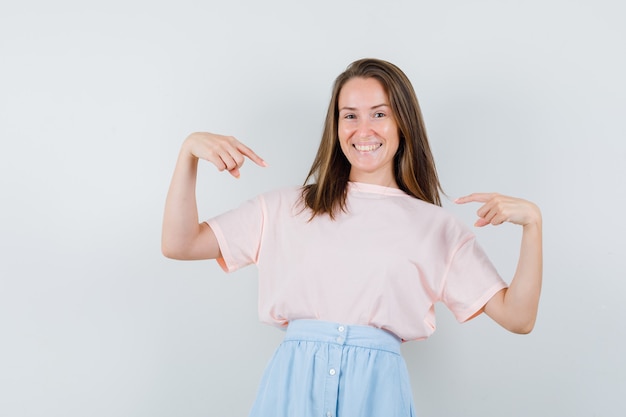 Foto grátis jovem fêmea apontando para si mesma em t-shirt, saia e parecendo com sorte. vista frontal.