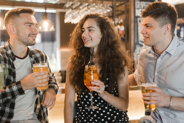 Jovem fêmea com dois amigos do sexo masculino segurando copos de bebidas