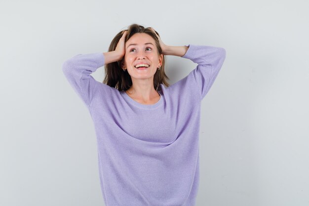 Jovem fêmea com uma blusa lilás de mãos dadas na cabeça enquanto ri e parece feliz