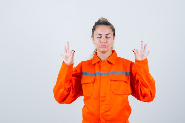 Foto grátis jovem fêmea com uniforme de trabalhador, meditando e olhando em silêncio, vista frontal.