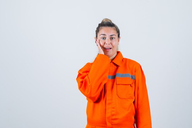 Jovem fêmea com uniforme de trabalhador, segurando a mão em sua bochecha e olhando com problemas, vista frontal.