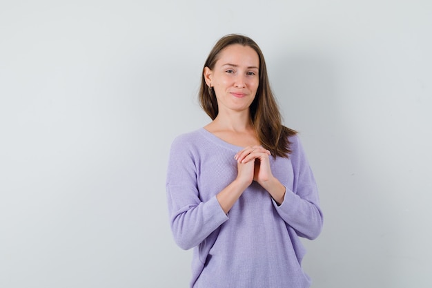 Jovem fêmea combinando as mãos no peito enquanto posava com uma blusa lilás e parecia relaxada. vista frontal.