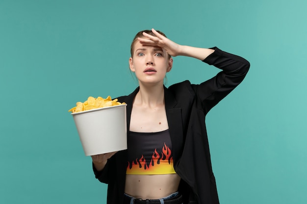 Foto grátis jovem fêmea comendo batata frita assistindo filme na superfície azul clara