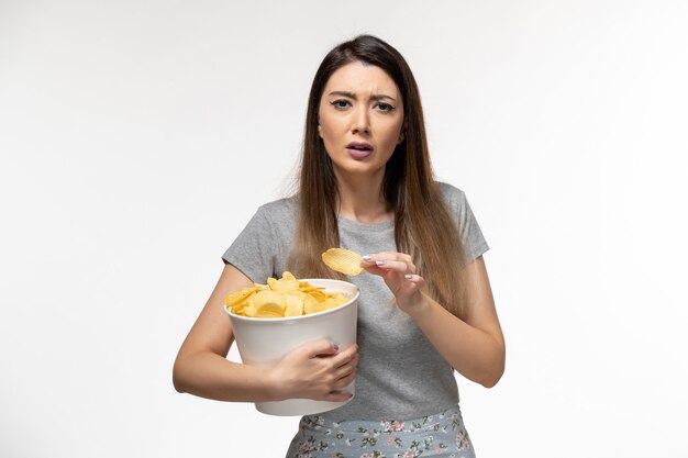 Jovem fêmea comendo batata frita enquanto assiste a um filme na superfície branca