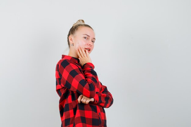 Jovem fêmea de camisa quadrada, posando de maneira pensativa e confiante, vista frontal.