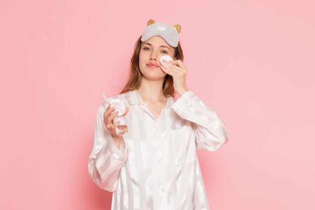 Jovem fêmea de pijama e máscara de dormir limpando o rosto rosa